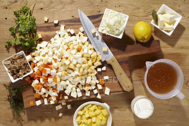 Ingredients for root vegetable soup on cutting board with knife over wooden surface — Stock Photo