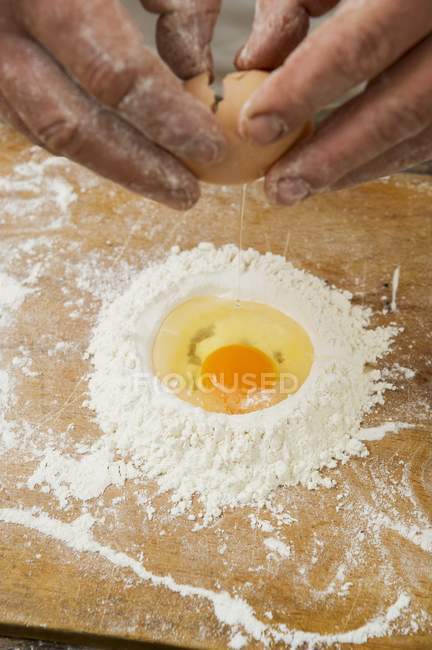 Visão cortada de mãos que freiam um ovo em uma pilha de farinha — Fotografia de Stock