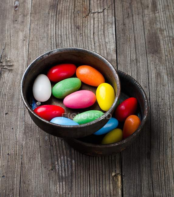 Colorful sugar eggs in ceramic bowls  on wooden surface — Stock Photo