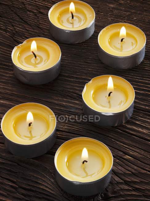Closeup view of six lit tealights on wooden surface — Stock Photo