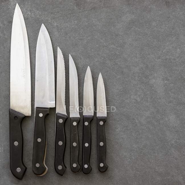 Closeup top view of assorted kitchen knives arranged in a row — Stock Photo