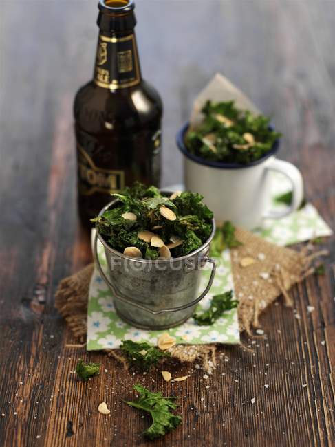 Зеленая капуста с миндалем и бутылкой пива на деревянной поверхности — стоковое фото