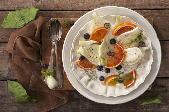 Фенхель і апельсиновий салат з чорницею на білій тарілці на рушник на дерев'яній поверхні — стокове фото