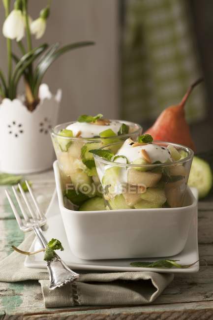 Салат з гострою грушею та огірком з м'ятою, кедровими горіхами та йогуртовим соусом у білій страві — стокове фото