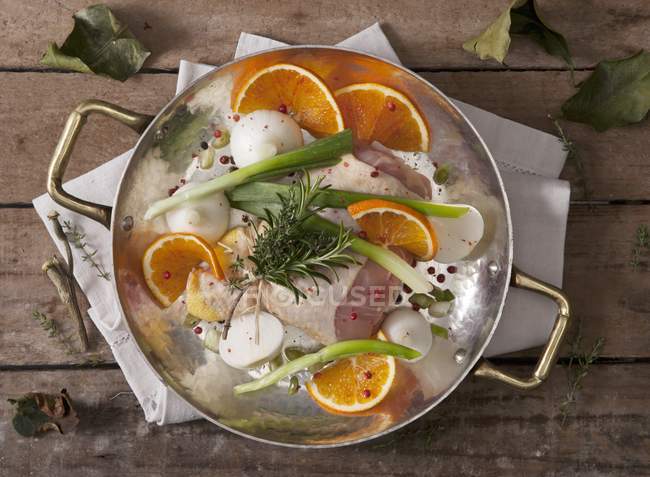 Chicken legs with onions, oranges and herbs in pan on wooden surface — Stock Photo