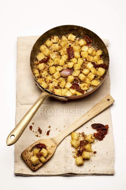 Fried potatoes with onions in pan over towel on white background — Stock Photo