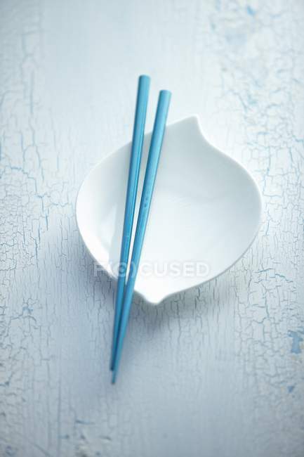 Erhöhte Ansicht blauer Essstäbchen auf weißer Schüssel und schäbig lackierter Oberfläche — Stockfoto