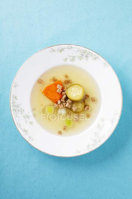 Brodo vegetale con crostini su piatto bianco su superficie blu — Foto stock
