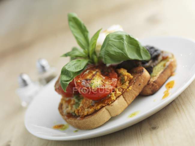 Bruschetta con tomates, champiñones y huevo escalfado en plato blanco - foto de stock