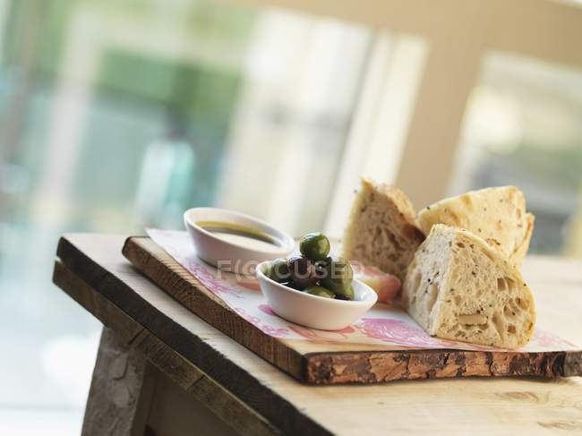 Оливки, хліб і олія на дерев'яній дошці над столом — стокове фото