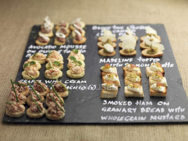 Elevated view of assorted canapes on black board with written labels — Stock Photo