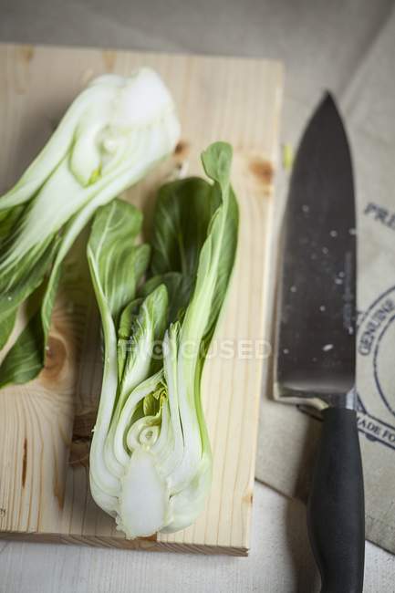 A hlaved bok choy on a wooden board with a knife — Stock Photo