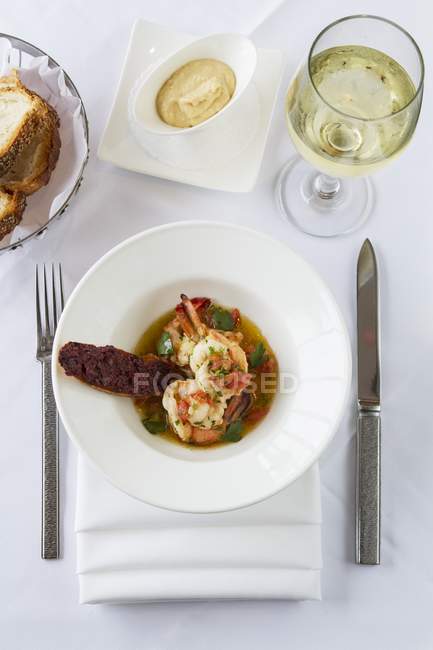 Sopa de mariscos con pan y vino en plato blanco sobre toalla sobre mesa con cuchillo y tenedor - foto de stock