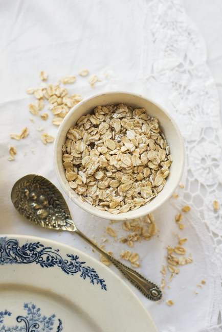 A bowl of porridge oats next to a vintage plate and spoon — Stock Photo