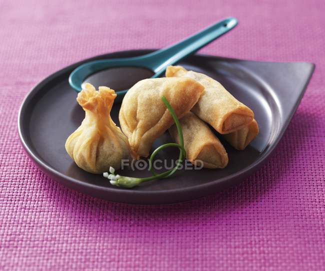 Closeup view of filled Asian Spring rolls with a sauce on a black plate — Stock Photo