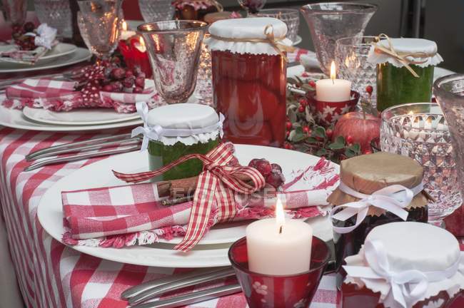Vue rapprochée de la table de Noël posée avec une nappe à carreaux rouges, des serviettes, des pots de confiture et des bougies — Photo de stock