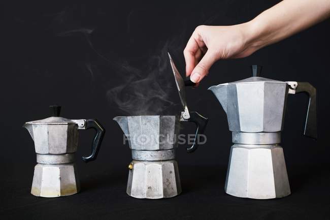 Vista de primer plano de la tapa de mano de la cafetera espresso vintage con café humeante - foto de stock