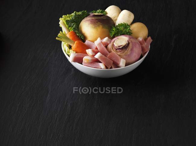 Una ciotola di verdure fresche con pancetta sulla superficie di legno nero — Foto stock