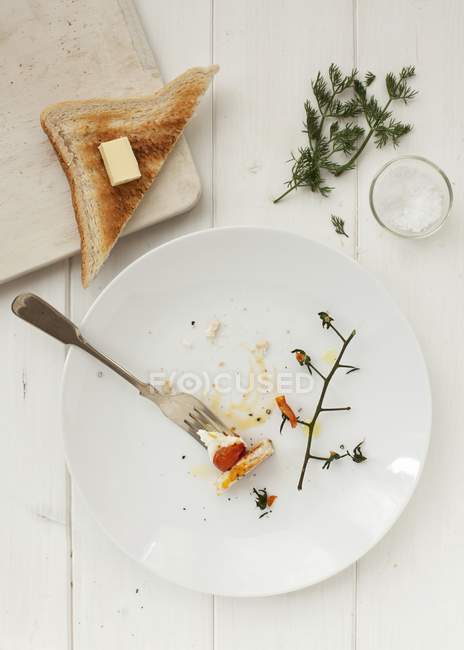 Остатки жареного яйца с помидорами и тостами на белой тарелке с вилкой — стоковое фото