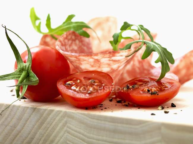 Tomates com fatias de salame e foguete sobre a superfície de madeira — Fotografia de Stock