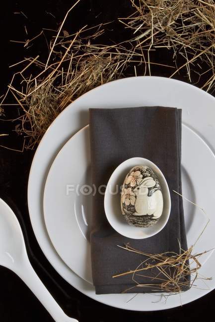 Vista superior de um cenário de lugar de Páscoa com um guardanapo cinza e um ovo pintado artisticamente — Fotografia de Stock