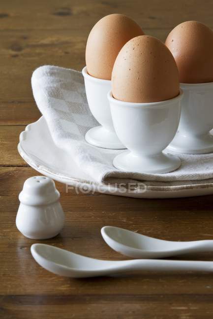 Closeup view of three brown eggs in white porcelain egg cups — Stock Photo