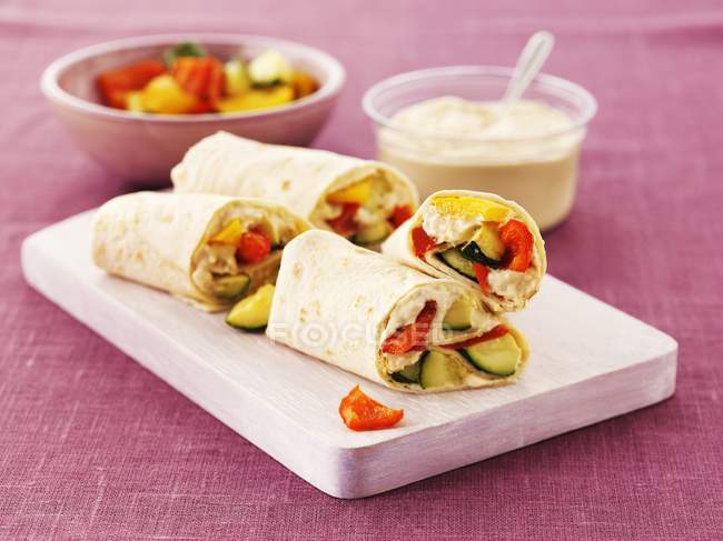 Wraps with hummus, cucumber and peppers on a board over pink surface — Stock Photo