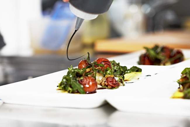 Tomato salad with rocket being drizzled with balsamic vinegar — Stock Photo