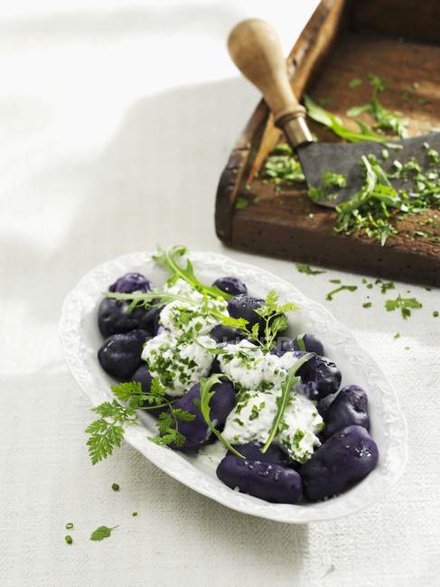Blue Congo potatoes with herb quark on white plate over white surface — Stock Photo