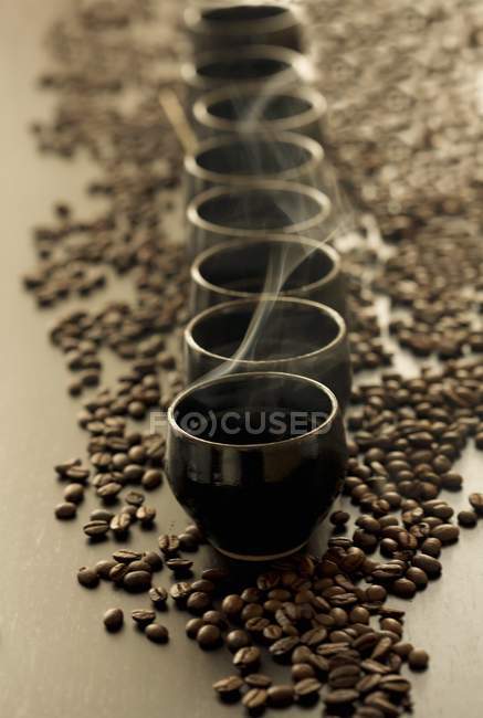 Vista de cerca de tazas de café al vapor en granos de café - foto de stock