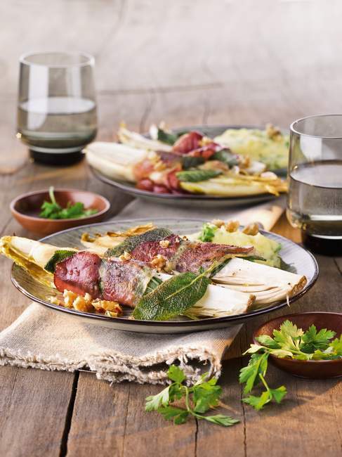 Chicory saltimbocca with raw ham and sage on plates over table — Stock Photo