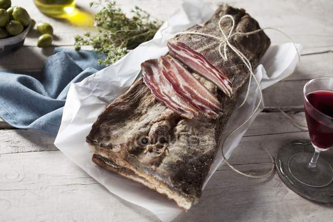 Bacon cru avec tranches sur morceau de papier — Photo de stock
