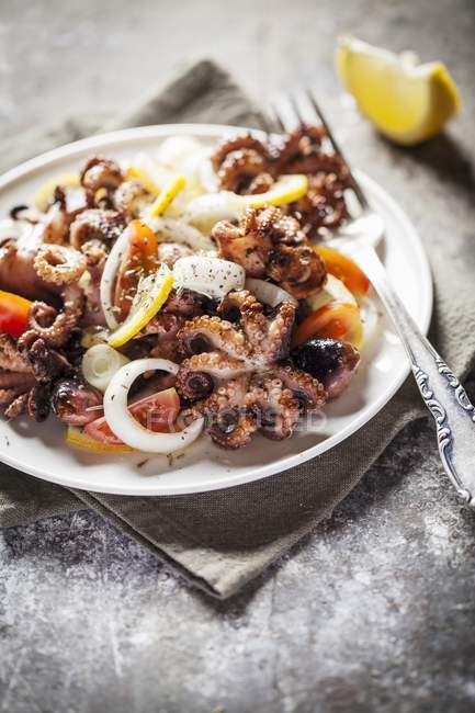 Salat mit Baby-Krake, Tomaten und Zwiebeln auf weißem Teller mit Gabel — Stockfoto