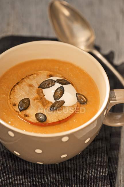 Apple and potato soup with pumpkin seeds in white bowl over towel with spoon — Stock Photo