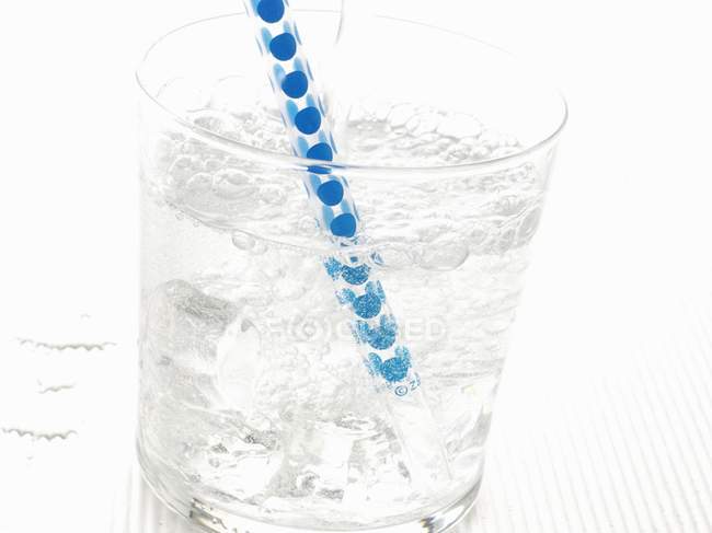 Closeup view of sparkling mineral water with ice cubes and straw in glass — Stock Photo