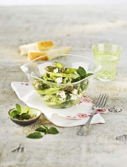 Salada de espargos verdes com sementes de gergelim e hortelã em tigela de vidro sobre toalha com garfo — Fotografia de Stock