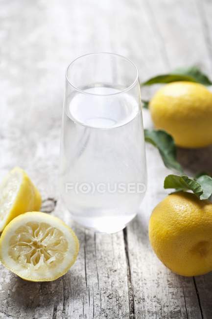 Bicchiere di acqua al limone e limoni — Foto stock