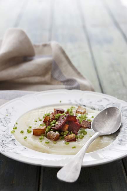 Cream of artichoke soup with roast potato and bacon on white plate with spoon — Stock Photo