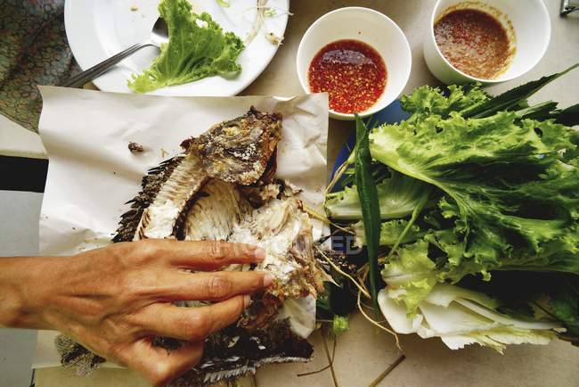 Cropped view of hand picking grilled tilapia piece with lettuce and sauces — Stock Photo