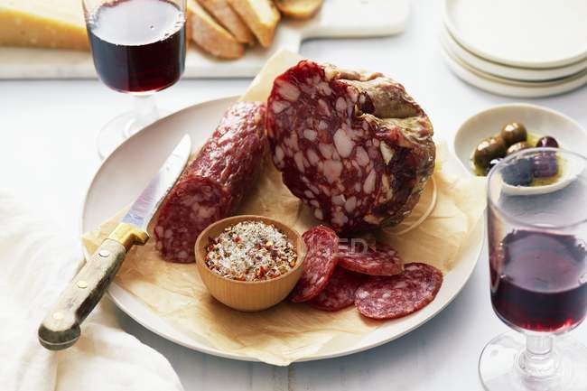 Salami mit Gewürzmischung, Rotwein und Oliven auf Teller mit Messer — Stockfoto