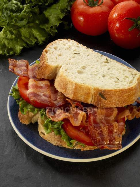 Крупним планом вид на хрусткий бекон, салат і бутерброд з помідорами на чорній тарілці — стокове фото
