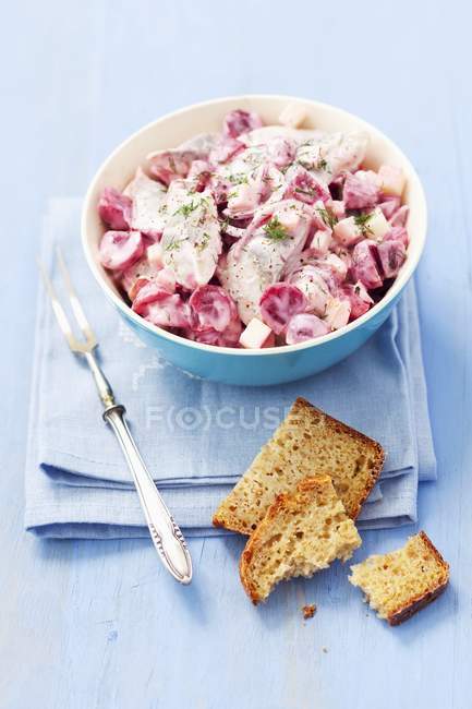 Closeup view of herring fish salad with beetroot, apple, red onions and mayonnaise in blue bowl over towel — Stock Photo