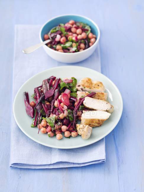Warm beetroot salad with chickpeas, onions, beetroot leaves and grilled chicken breast on white plate over towel — Stock Photo