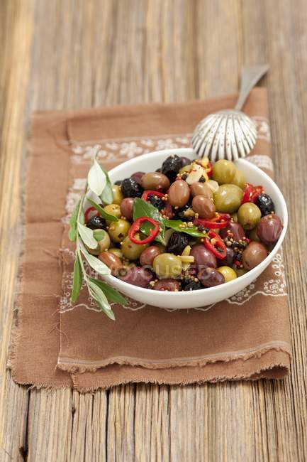 Olive marinate miste con aglio, senape e peperoncino su piatto bianco sopra asciugamano — Foto stock