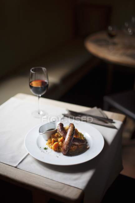 Salsicce belghe con verdure pure su piatto bianco sopra tavolo con bicchiere di vino — Foto stock