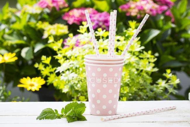 Vue rapprochée de trois tasses en papier rose et de pailles assorties sur une table de jardin — Photo de stock