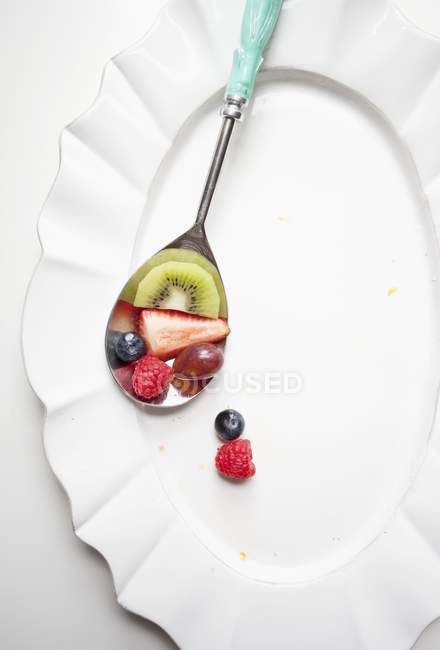 Close-up vista superior de pedaços de frutas na colher e prato branco — Fotografia de Stock