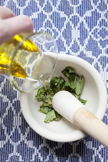 Hand gießt Olivenöl in Basilikum — Stockfoto