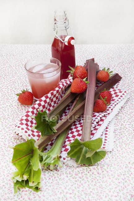 Vue rapprochée de bouteille de rhubarbe et sirop de fraise et dans un verre avec de l'eau pétillante — Photo de stock