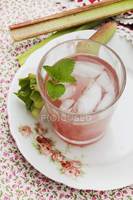 Closeup view of rhubarb Spritzer with ice cubes in glass and pieces of rhubarb on rose patterned plate — Stock Photo